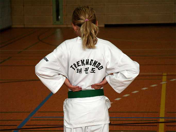 Rückansicht einer Taekwondo-Schülerin (Mädchen) im Trainingsanzug (Dobok) mit grünem Gürtel