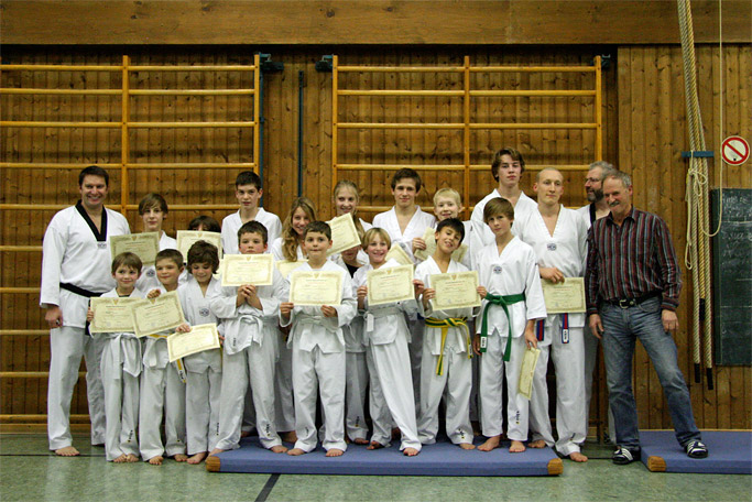 Prüfungsfoto in der Mehrzweck-Turnhalle von Bad Tölz mit
        Trainer Willi Hobel und geprüften Kindern und Jugendlichen im
        Taekwondo-Trainingsanzug (Tobok)